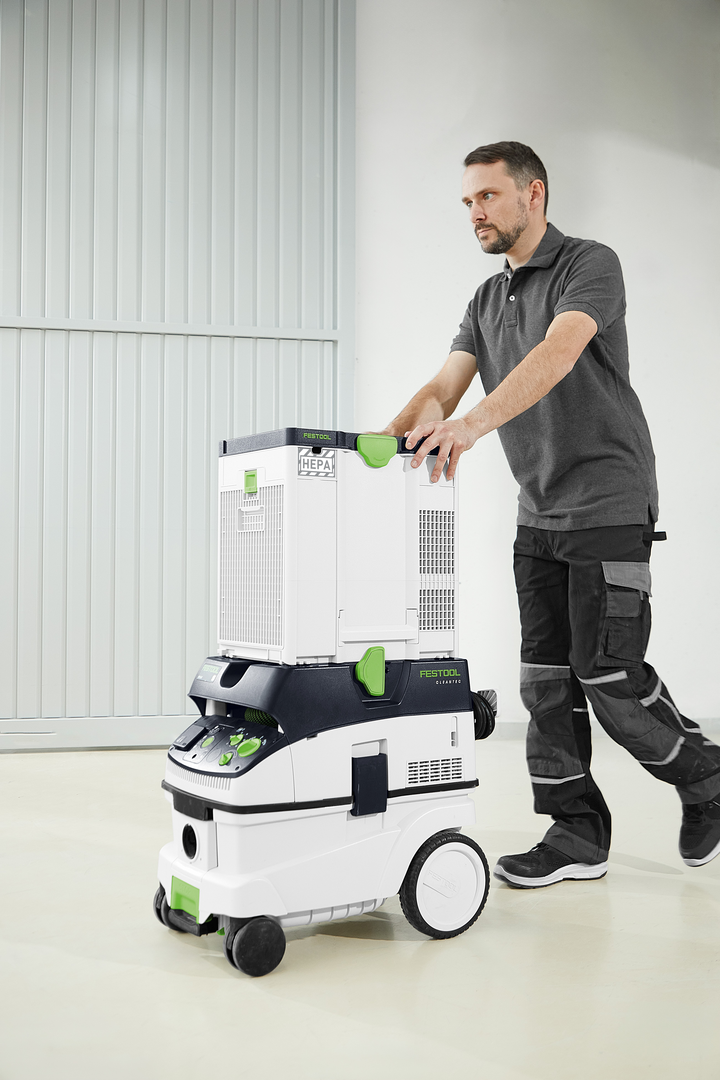 Man moving a Festool air filtration and dust extraction unit on a smooth workshop floor for dust management