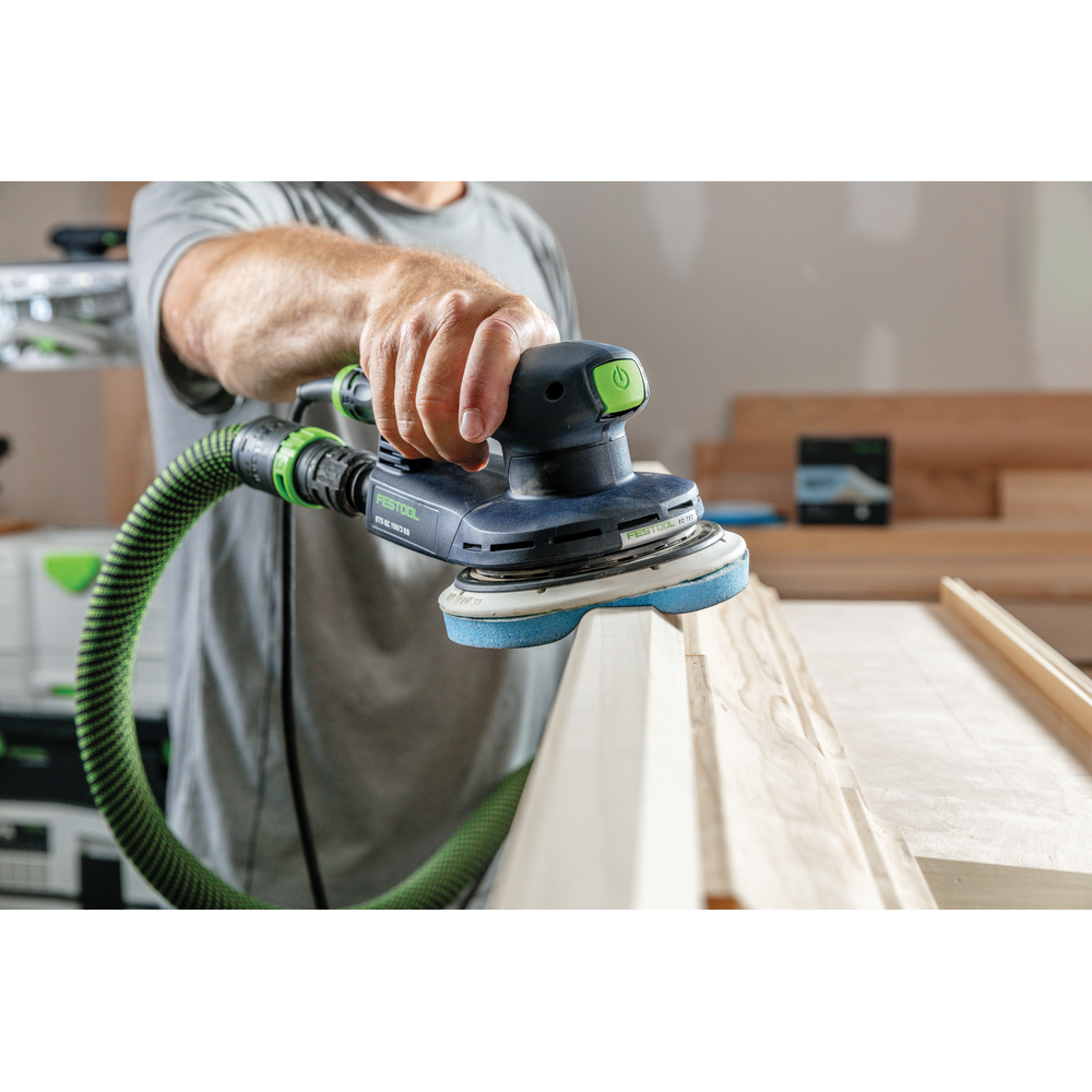 Worker using Festool power sander with blue abrasive disc smoothing wooden molding in home improvement tool accessories setting