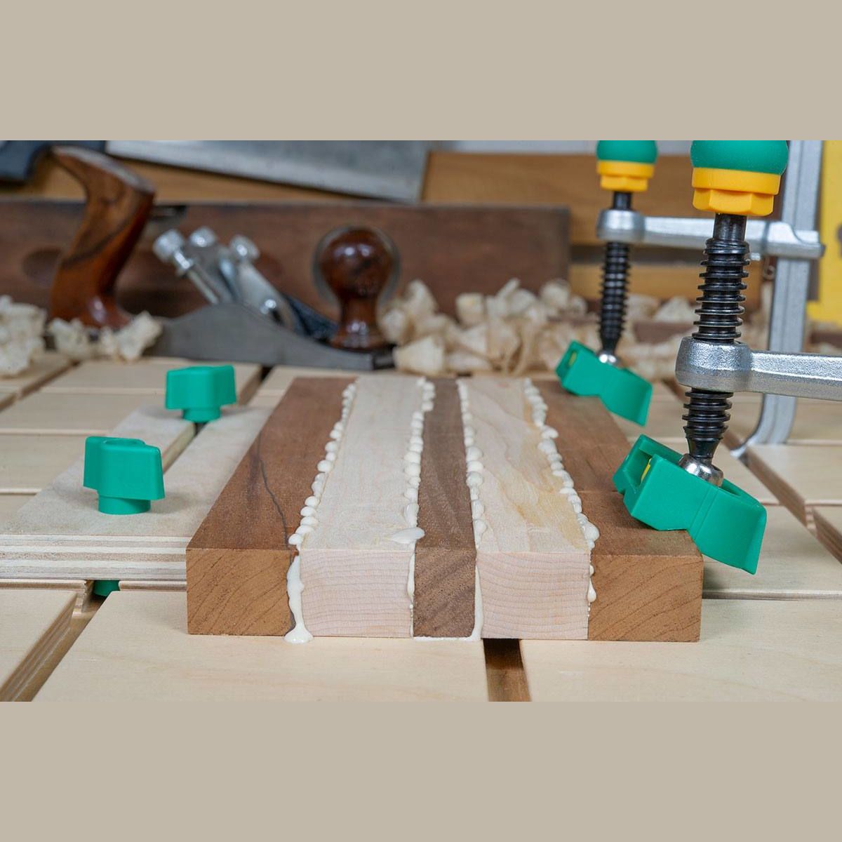 Woodworking clamp with green handles securing glued wooden boards on a dovetail track for precise assembly tasks