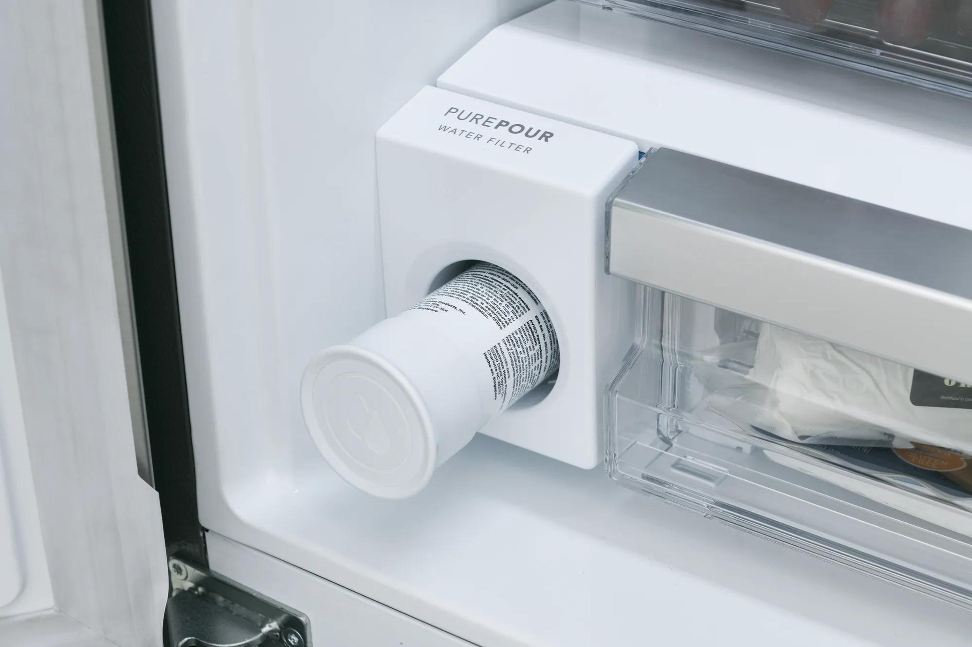 Close-up of refrigerator water filter installed inside door near clear food storage compartment in kitchen appliance setting
