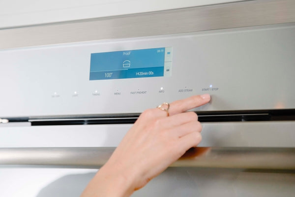 Hand pressing start button on stainless steel wall oven digital control panel from Thermador Appliances collections