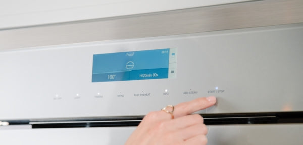 Finger pressing electronic control button on stainless steel Thermador wall oven with digital display panel