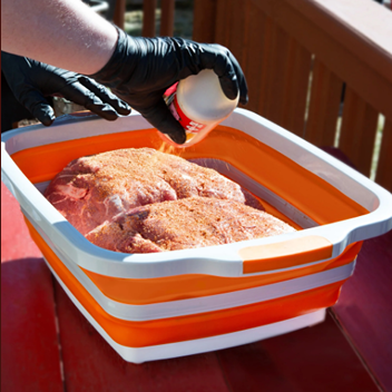 Collapsible orange prep tub used for seasoning large cuts of raw meat in outdoor grilling accessories setting
