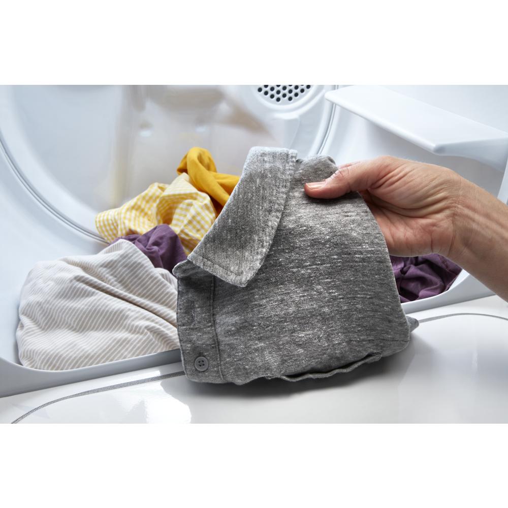 Hand removing gray shirt from inside large capacity top load gas dryer in laundry room setting