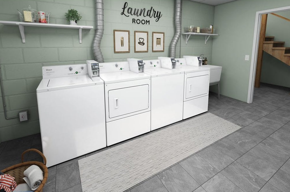 Four white coin-operated laundry machines including electric dryers and washers in a gray-tiled laundry room
