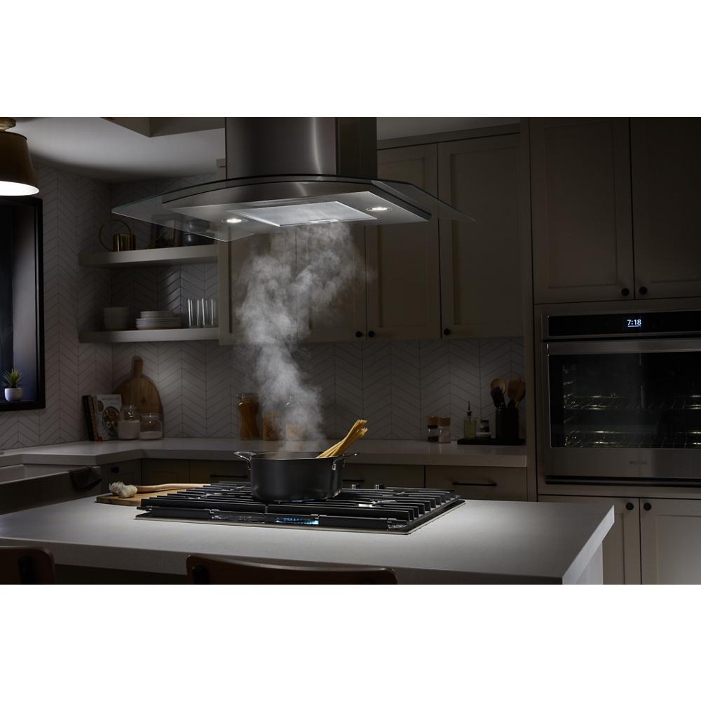 Stainless steel chimney range hood ventilating steam from pot on gas cooktop in modern kitchen and appliances setting