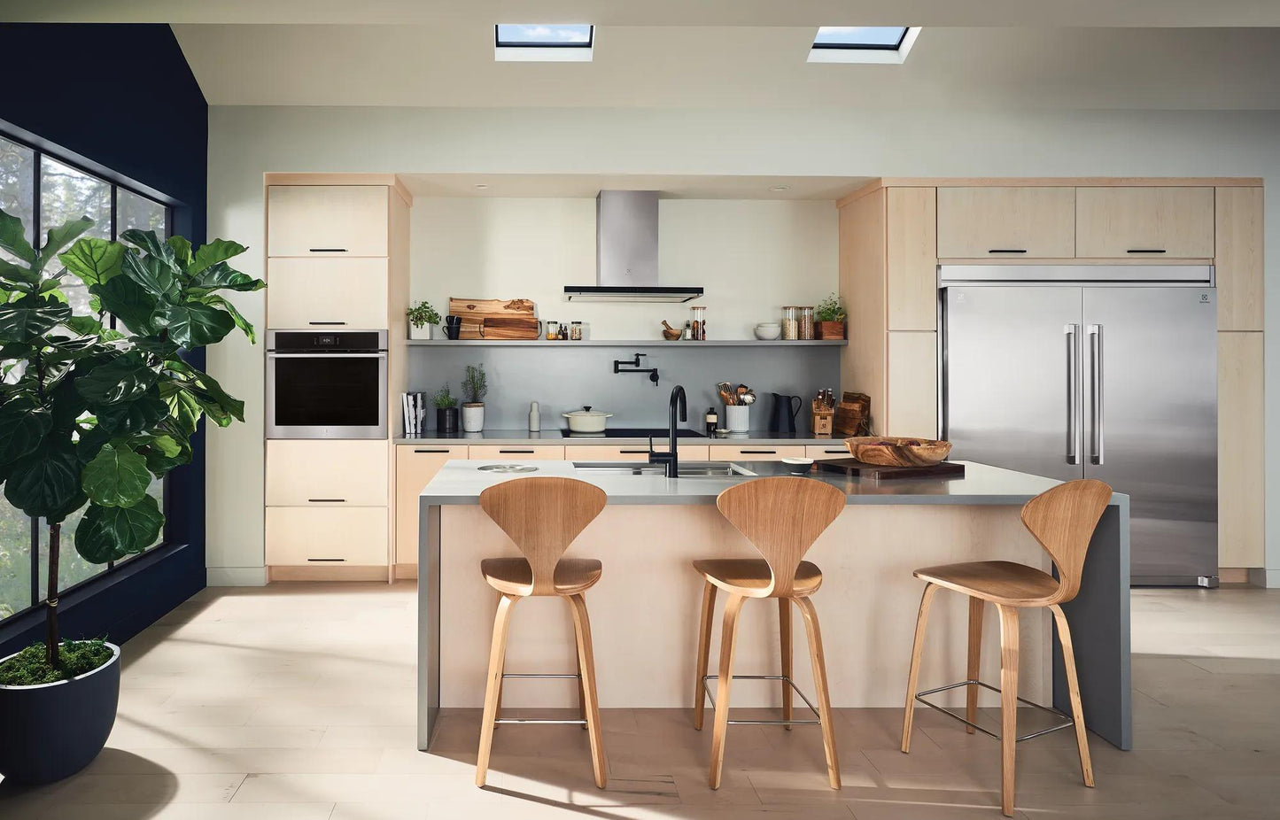 Modern kitchen featuring built-in stainless steel electric wall ovens and integrated appliances with wood cabinetry and island seating