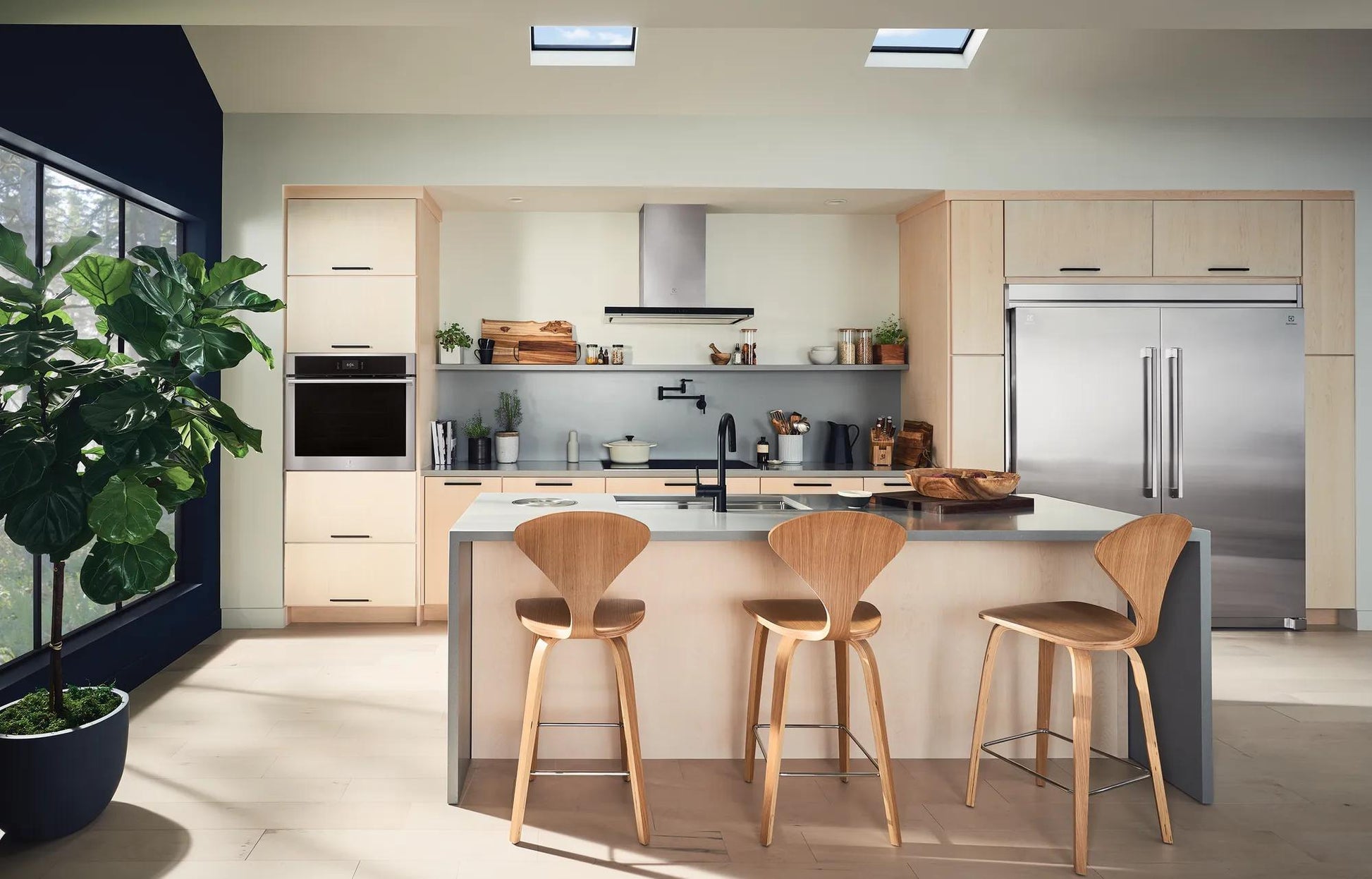 Modern kitchen featuring built-in stainless steel electric wall ovens and integrated appliances with wood cabinetry and island seating