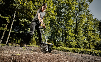 Person using DEWALT cultivator attachment with steel tines on soil in outdoor garden setting from Dewalt Outdoor Power collection