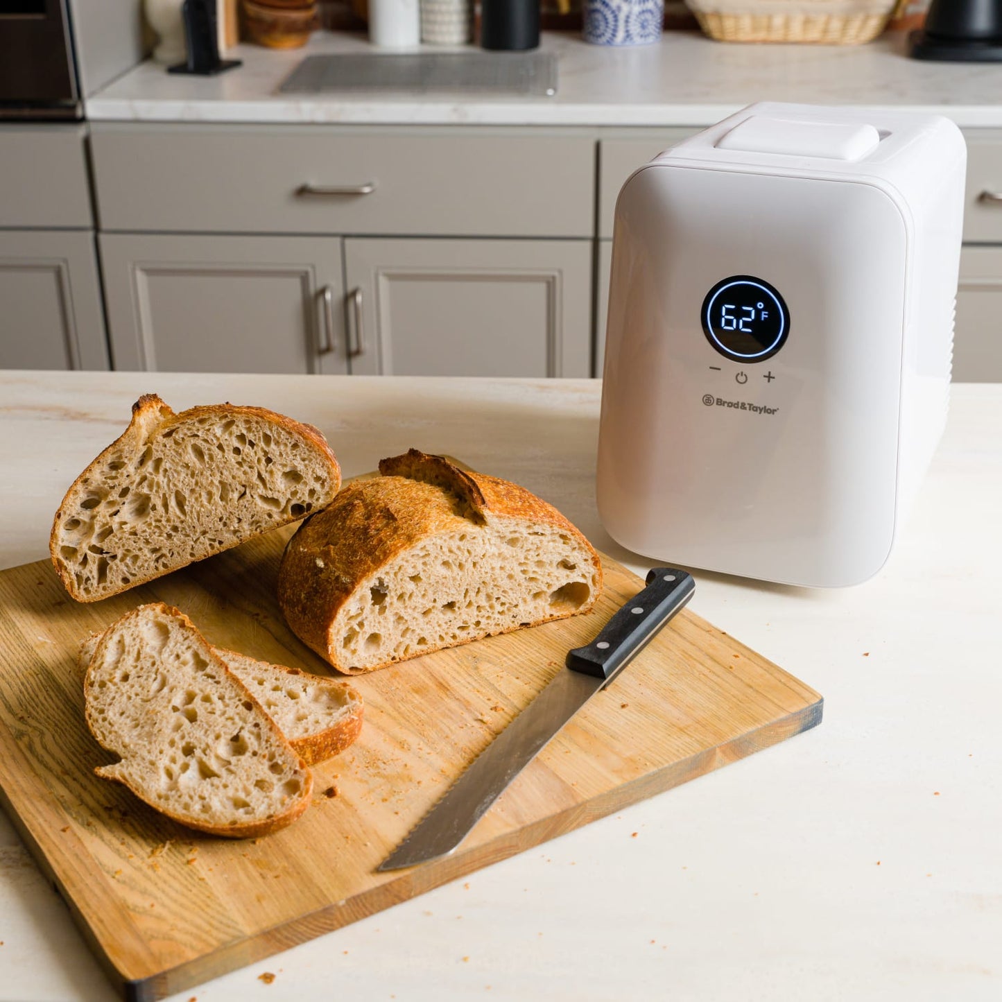 Compact white appliance with 62°F digital display beside sliced artisan bread on wooden cutting board in kitchen setting