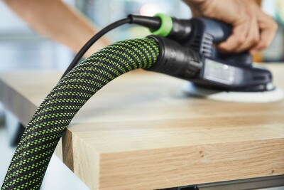 Green and black flexible anti-static hose connected to a power sander on a wooden surface in woodworking tools collection
