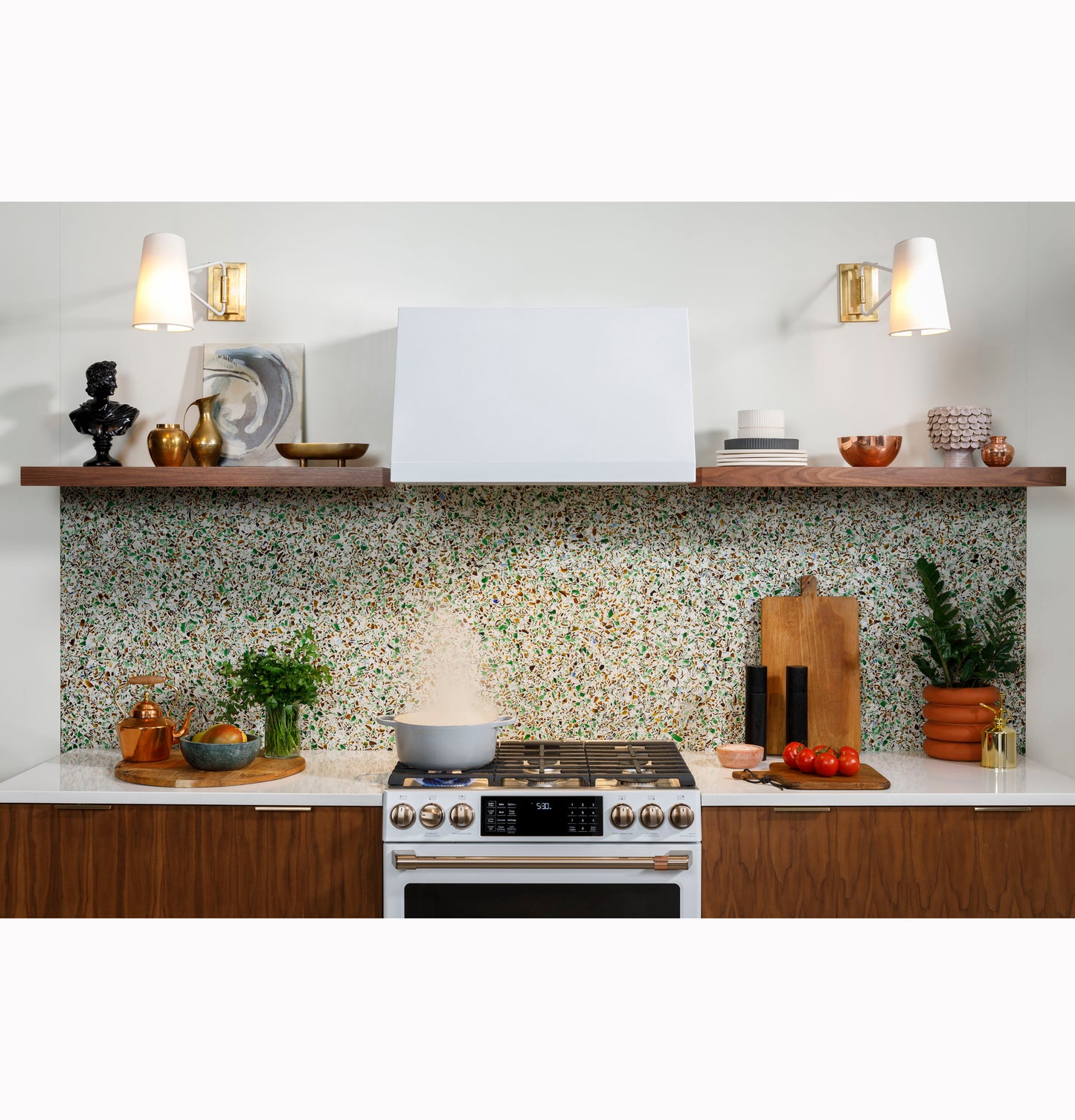 Modern kitchen with wood cabinetry, terrazzo backsplash, cooking range, and commercial style white range hood in appliances setting