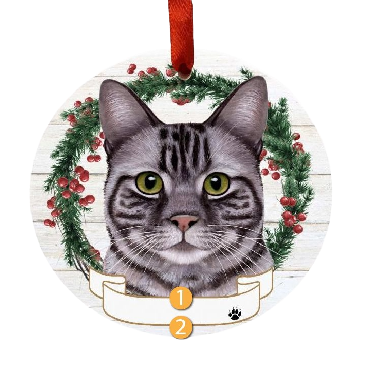 Round Christmas ornament featuring a silver tabby cat face inside a festive wreath with red berries and pine needles