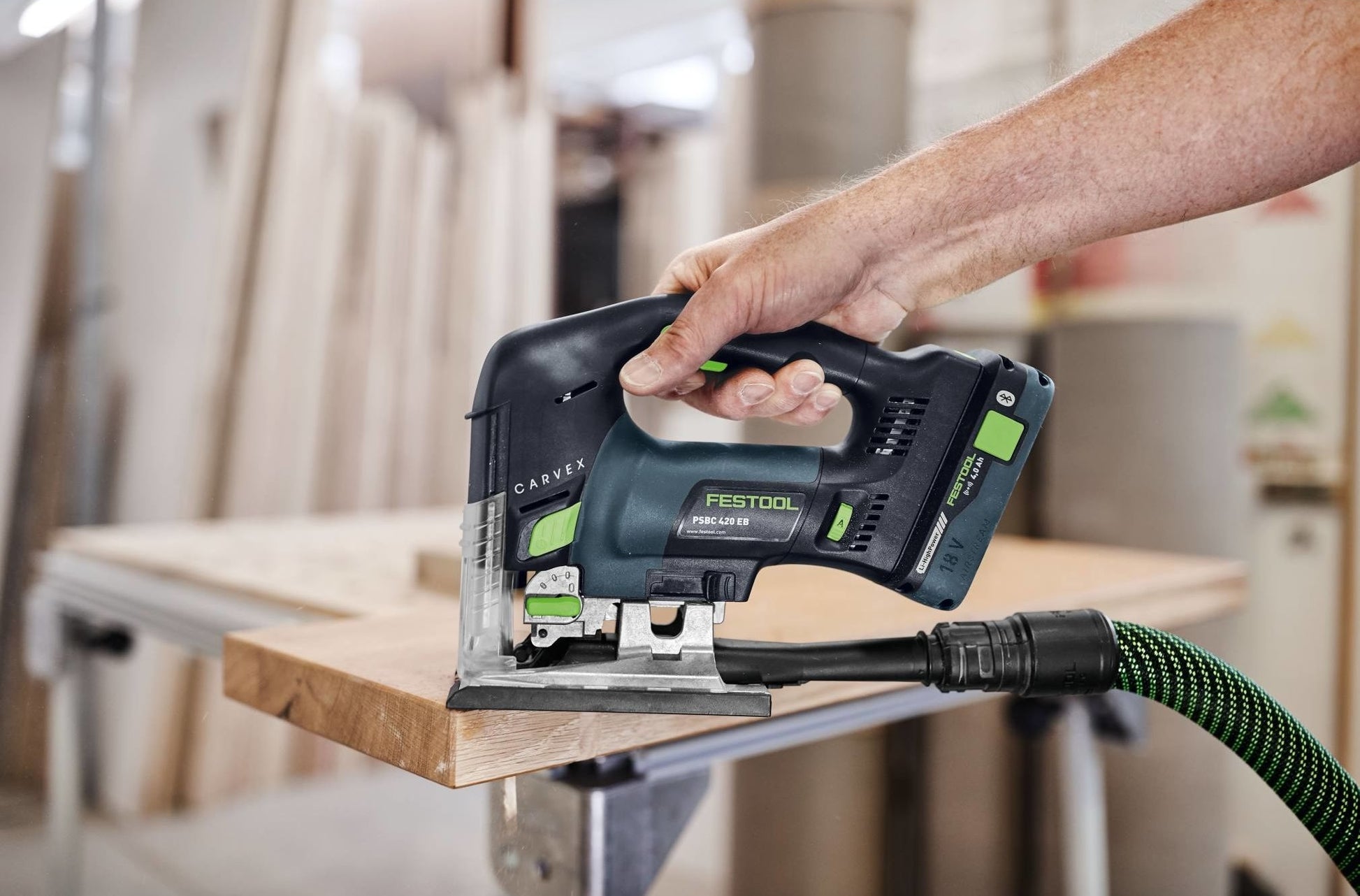 Cordless D-handle jigsaw cutting wood on workbench, power tool in workshop for home improvement tasks