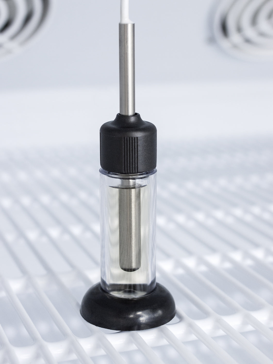 Close-up of temperature probe sensor with black base resting on white shelving inside a medical refrigerator interior