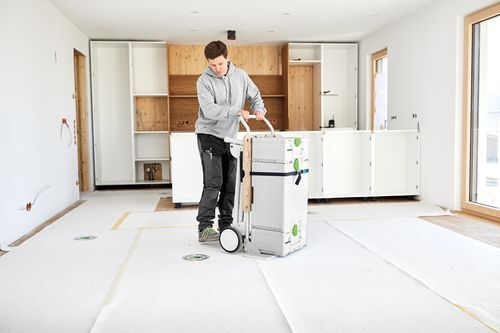 Man maneuvering a Festool cordless table saw in a bright home improvement space with installed kitchen cabinets nearby