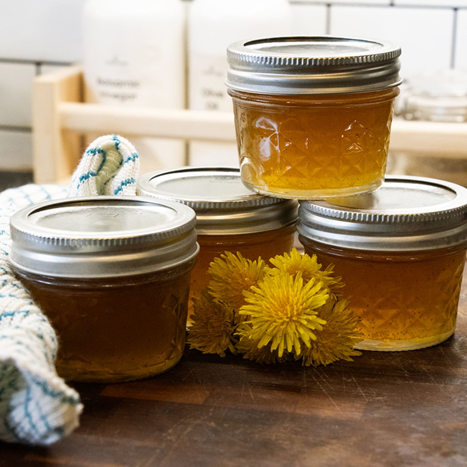 Four clear 4 oz. glass jars with silver lids filled with golden homemade jam on wooden surface with yellow flowers