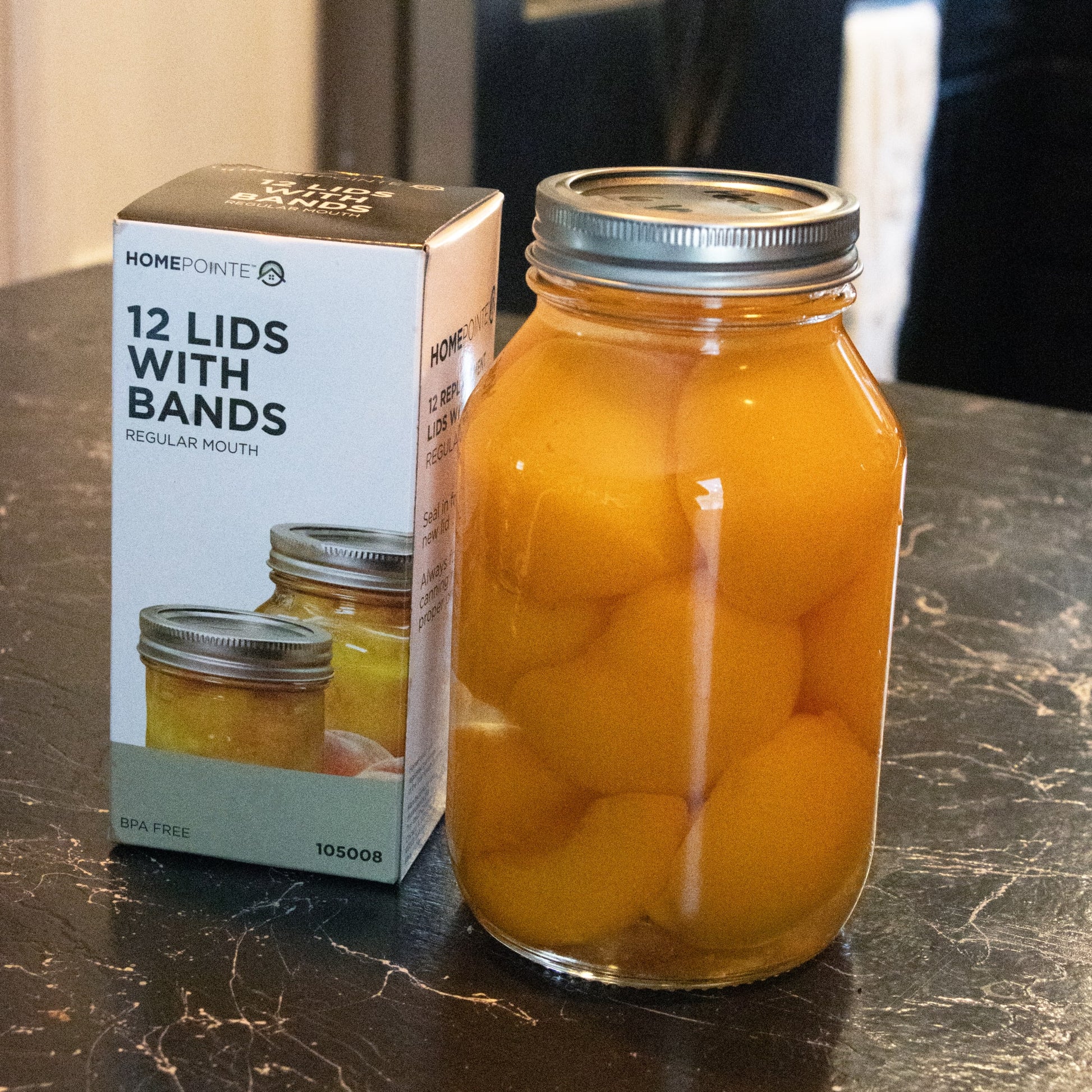 Box of 12 silver lids with bands next to glass jar filled with preserved peaches in kitchenware under $50 collection