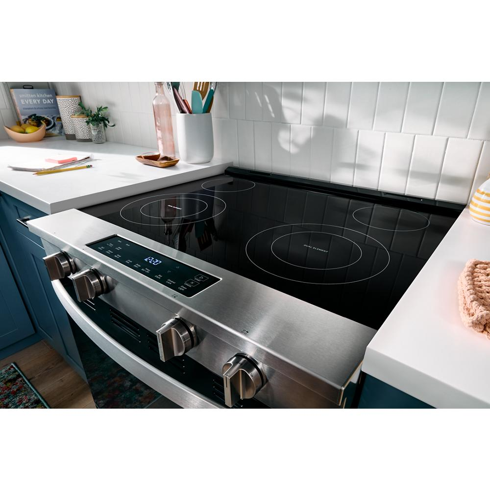 Stainless steel electric range with smooth black ceramic cooktop and front control knobs in a modern kitchen setting