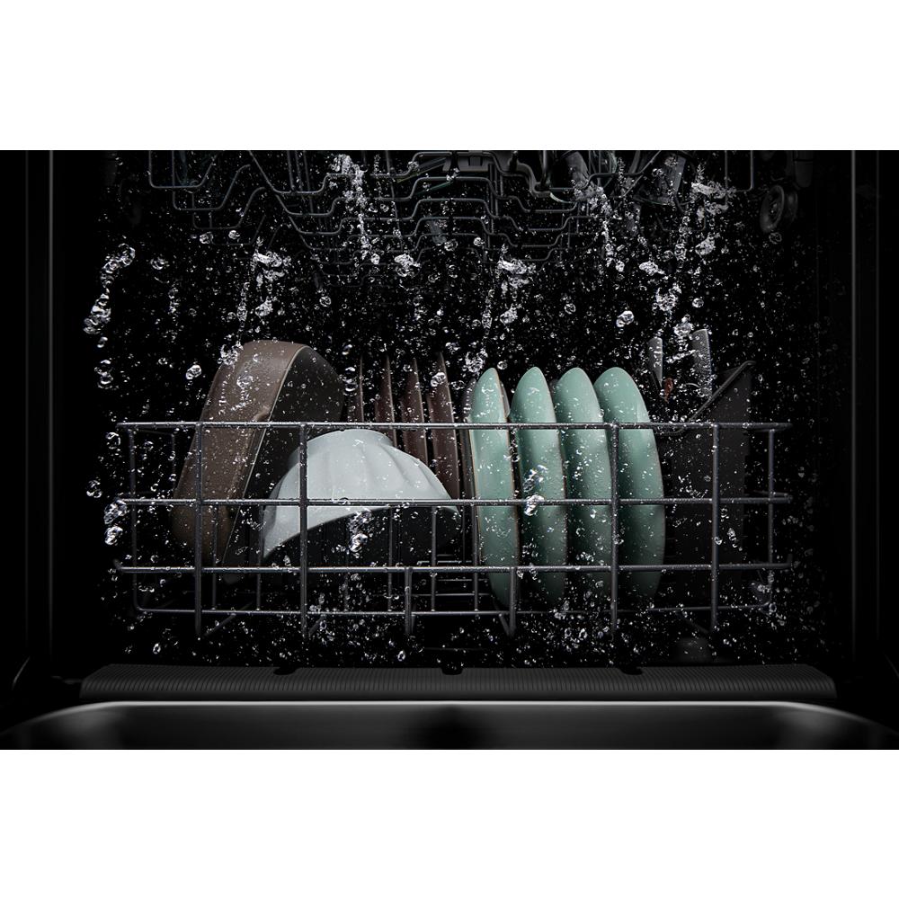 Water spraying inside dishwasher rack loaded with various clean plates in dark kitchen appliance setting