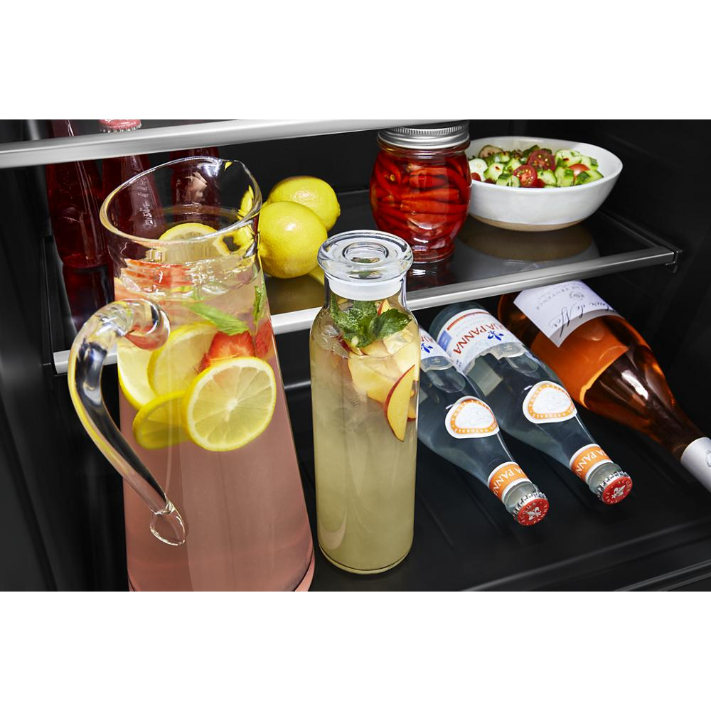 Undercounter refrigerator interior with glass door showing beverages, lemons, jar, salad bowl, and bottles in KitchenAid appliances collection