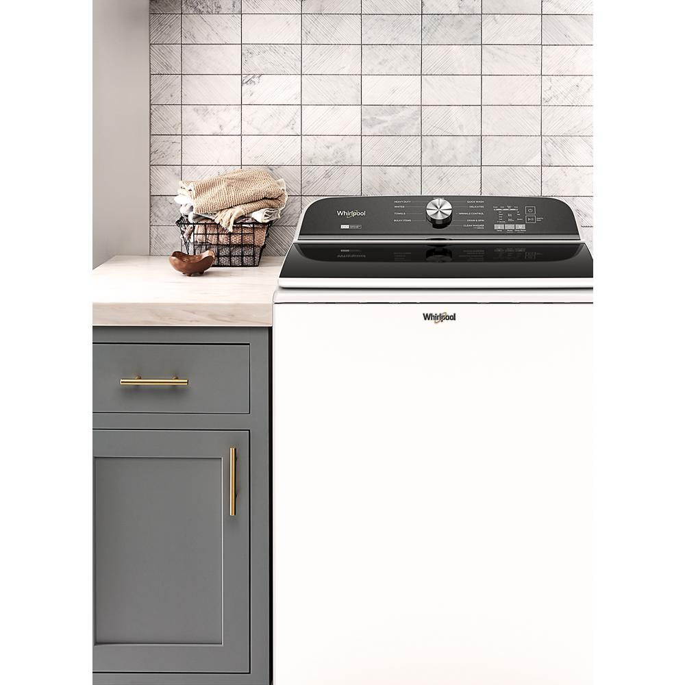 White top load washer with digital controls next to gray cabinetry and a wire basket with towels in a laundry room setting