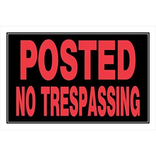 Black sign with bold red lettering stating posted no trespassing for property protection and security use
