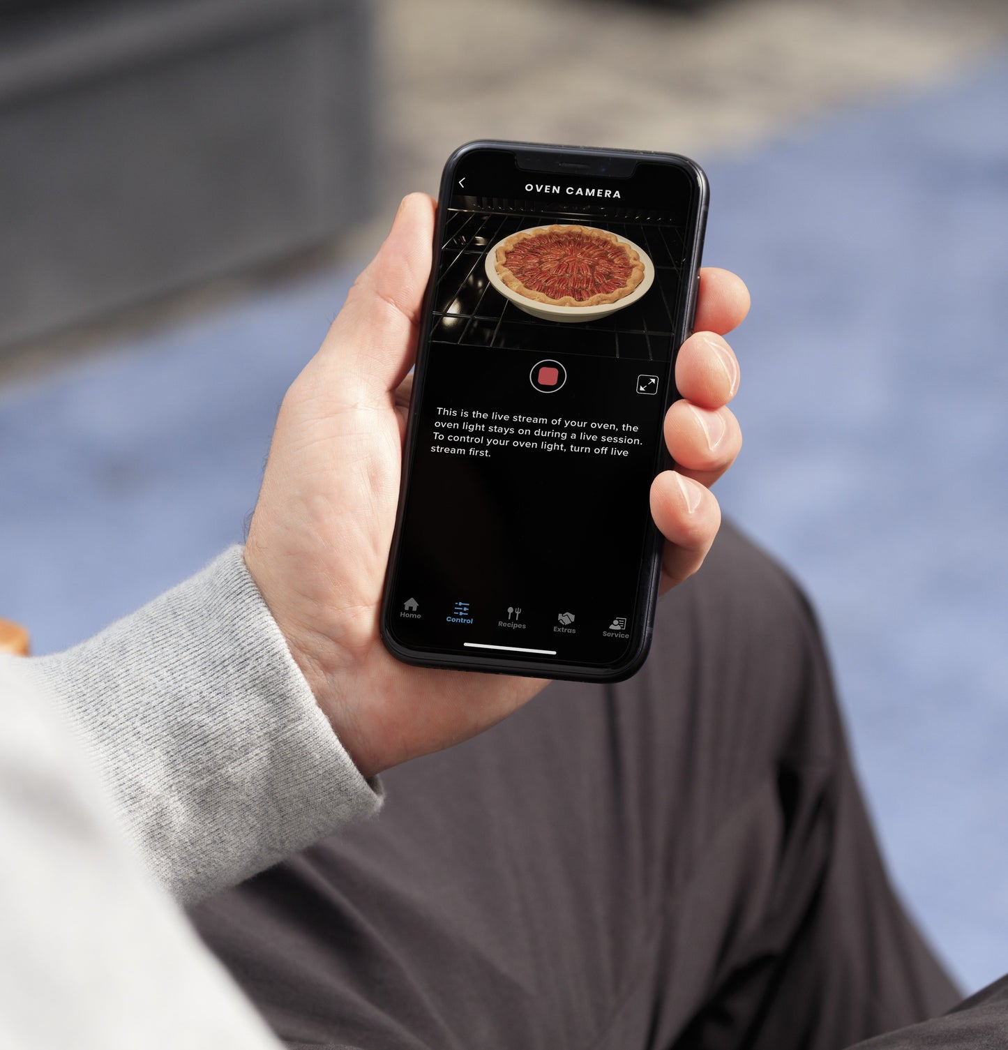 Person holding smartphone showing live oven camera view with pizza inside smart double wall oven for home improvement