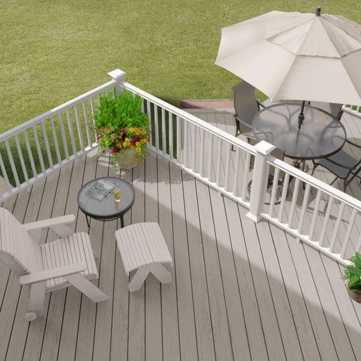 Outdoor deck with composite boards and white railing, featuring seating and table under beige umbrella in home improvement setting