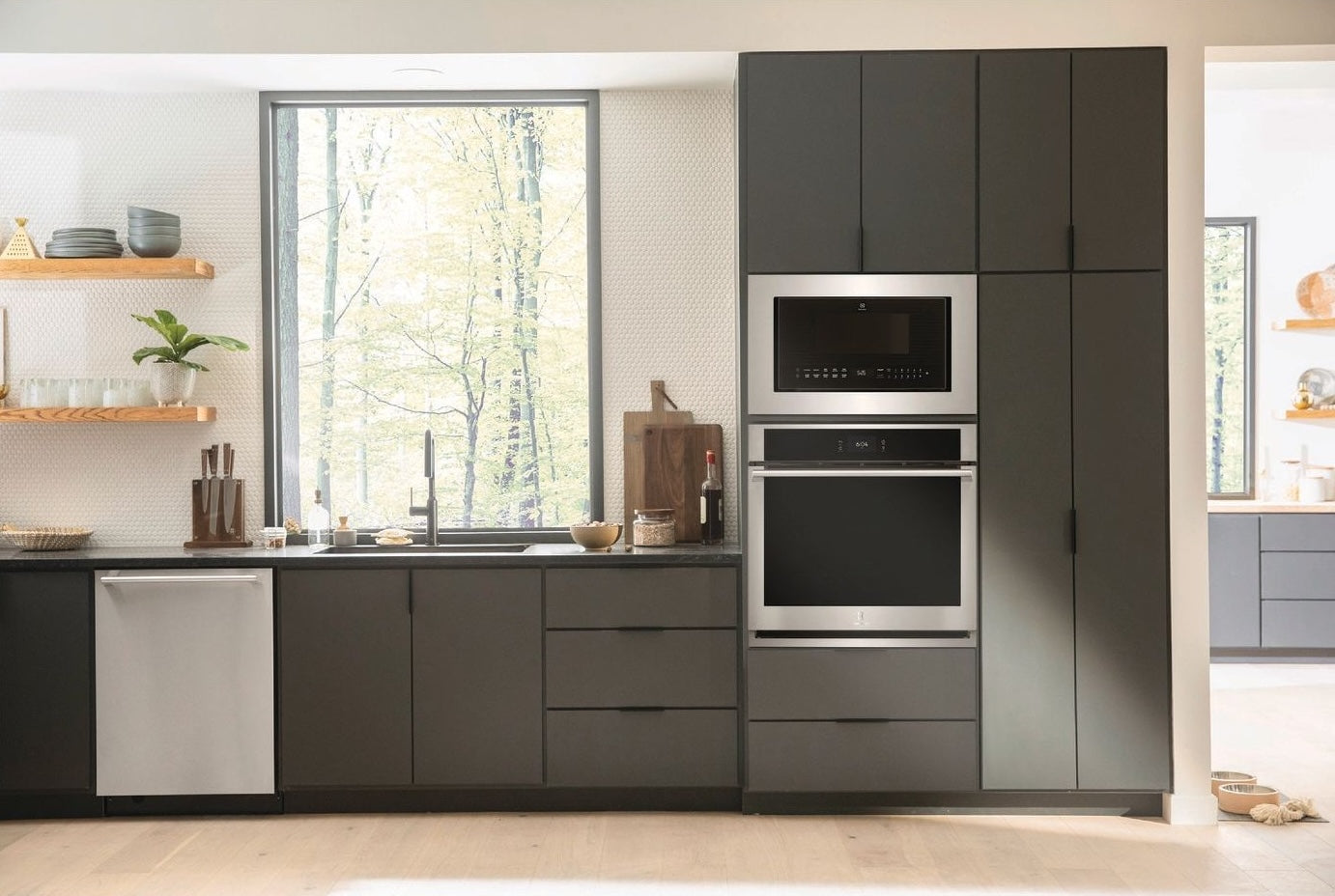 Modern kitchen with built-in microwave and oven in dark cabinetry, featuring large window and minimalist decor elements.
