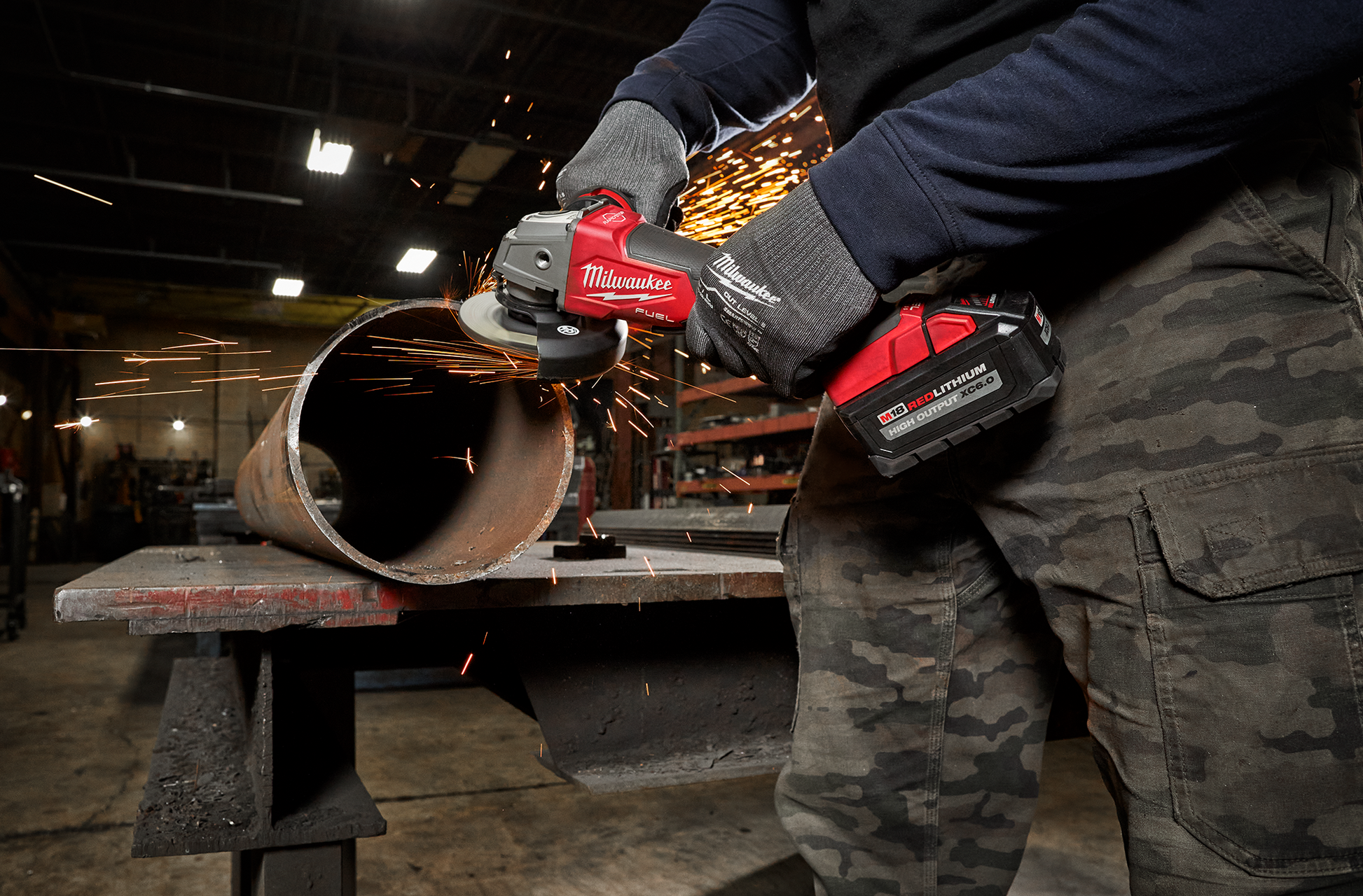 Worker using red cordless grinder to cut metal pipe in industrial workshop for power tools and home improvement