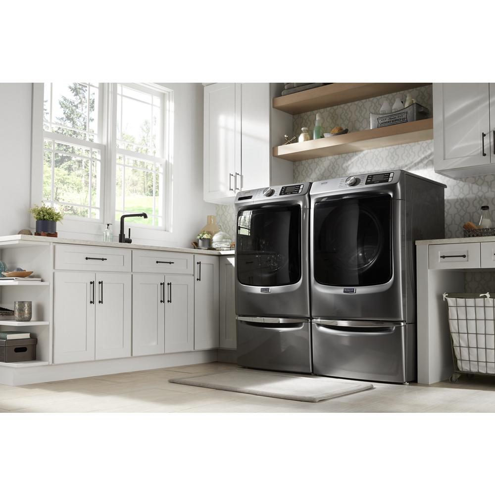 Modern laundry room with matching front load washer and dryer elevated on dark storage pedestals near white cabinetry