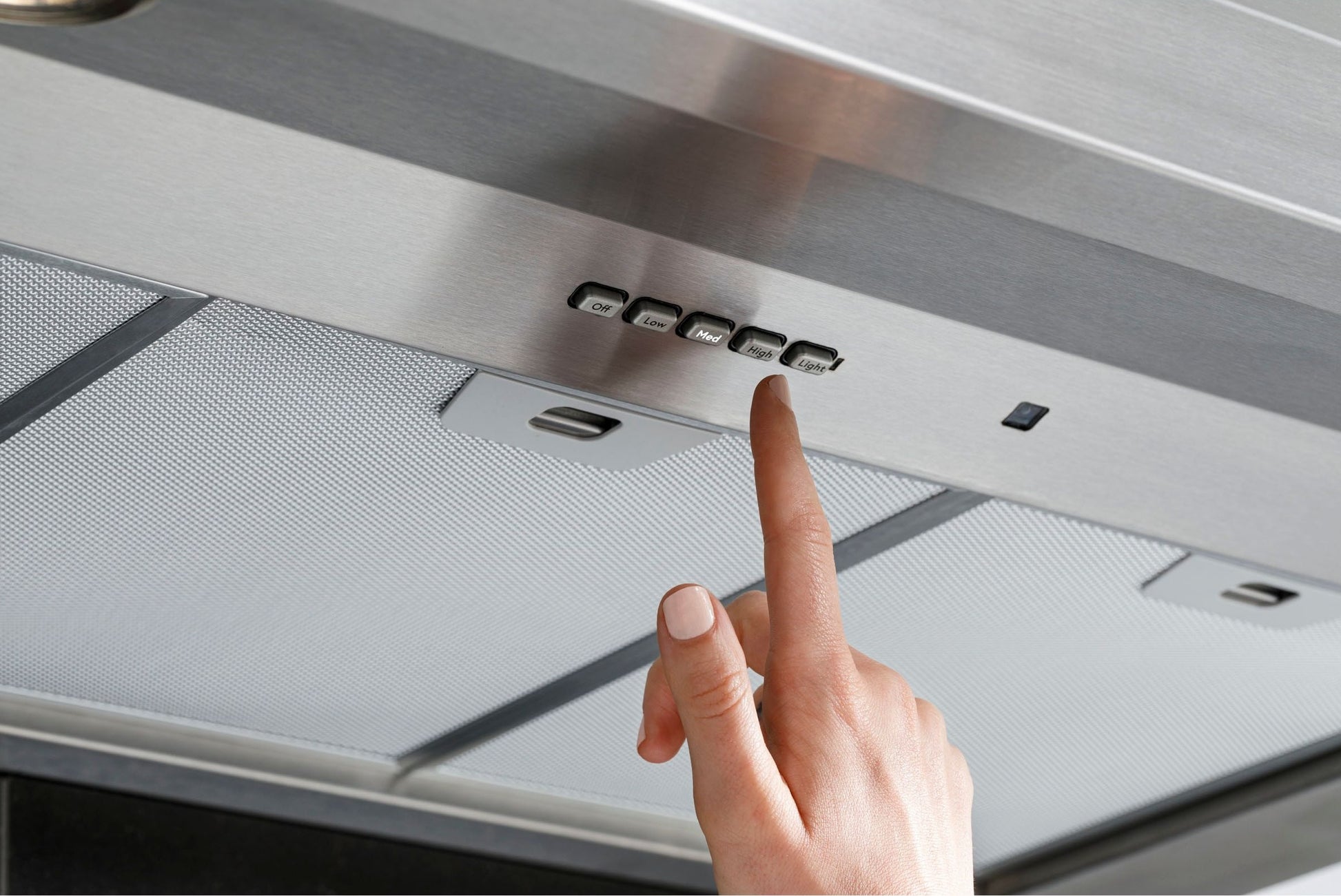 Hand pressing control button on stainless steel commercial range hood from kitchen appliances collection
