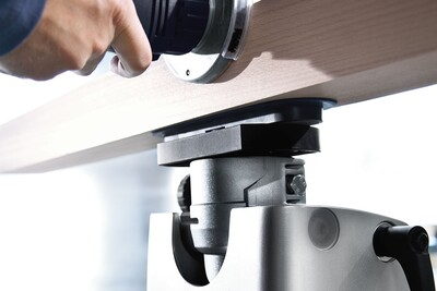 Close-up of a person using a plunge router on a wooden board, focusing on the router base and adjustment mechanism during a home improvement task.