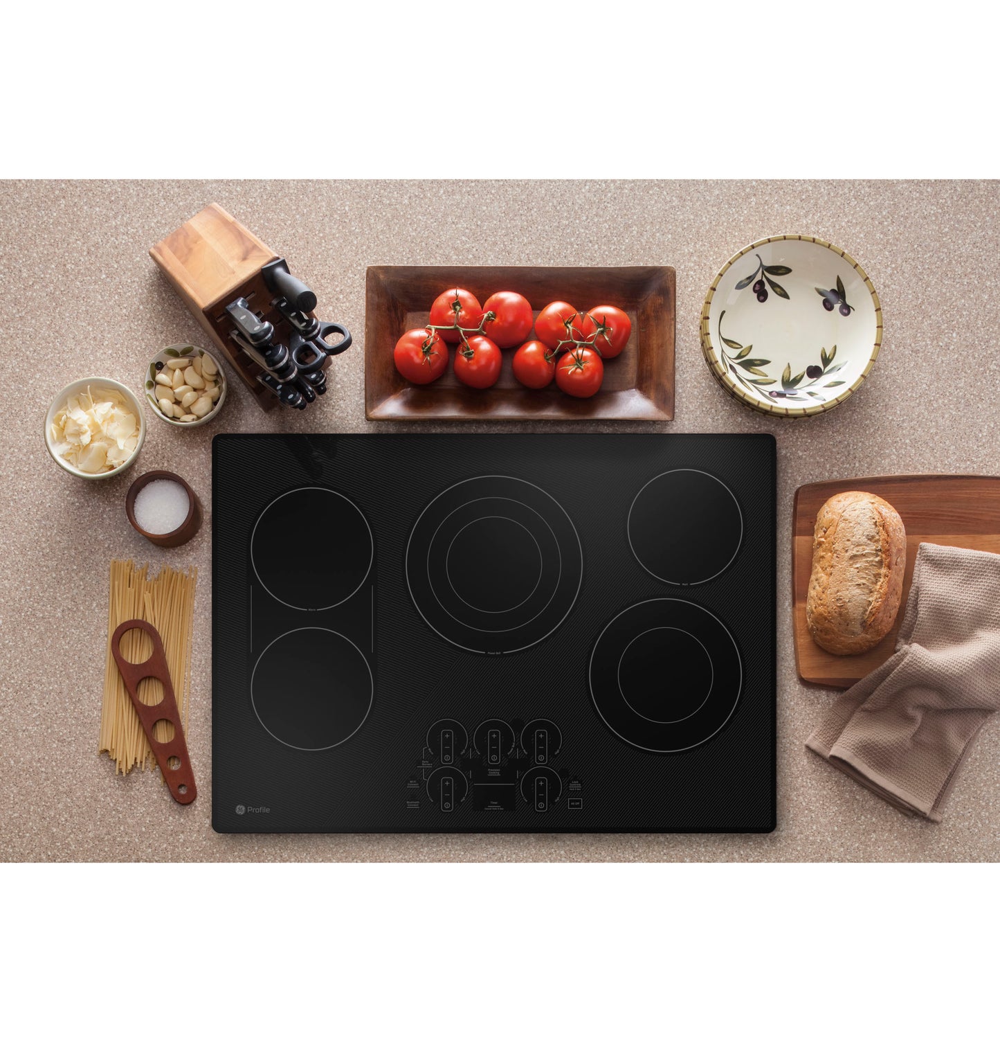Black built-in electric cooktop with touch controls, surrounded by kitchenware and fresh ingredients on countertop