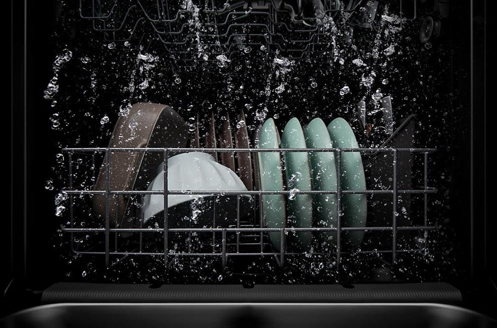 Interior view of dishwasher rack filled with dishes mid-washing cycle showcasing water spray and cleaning action