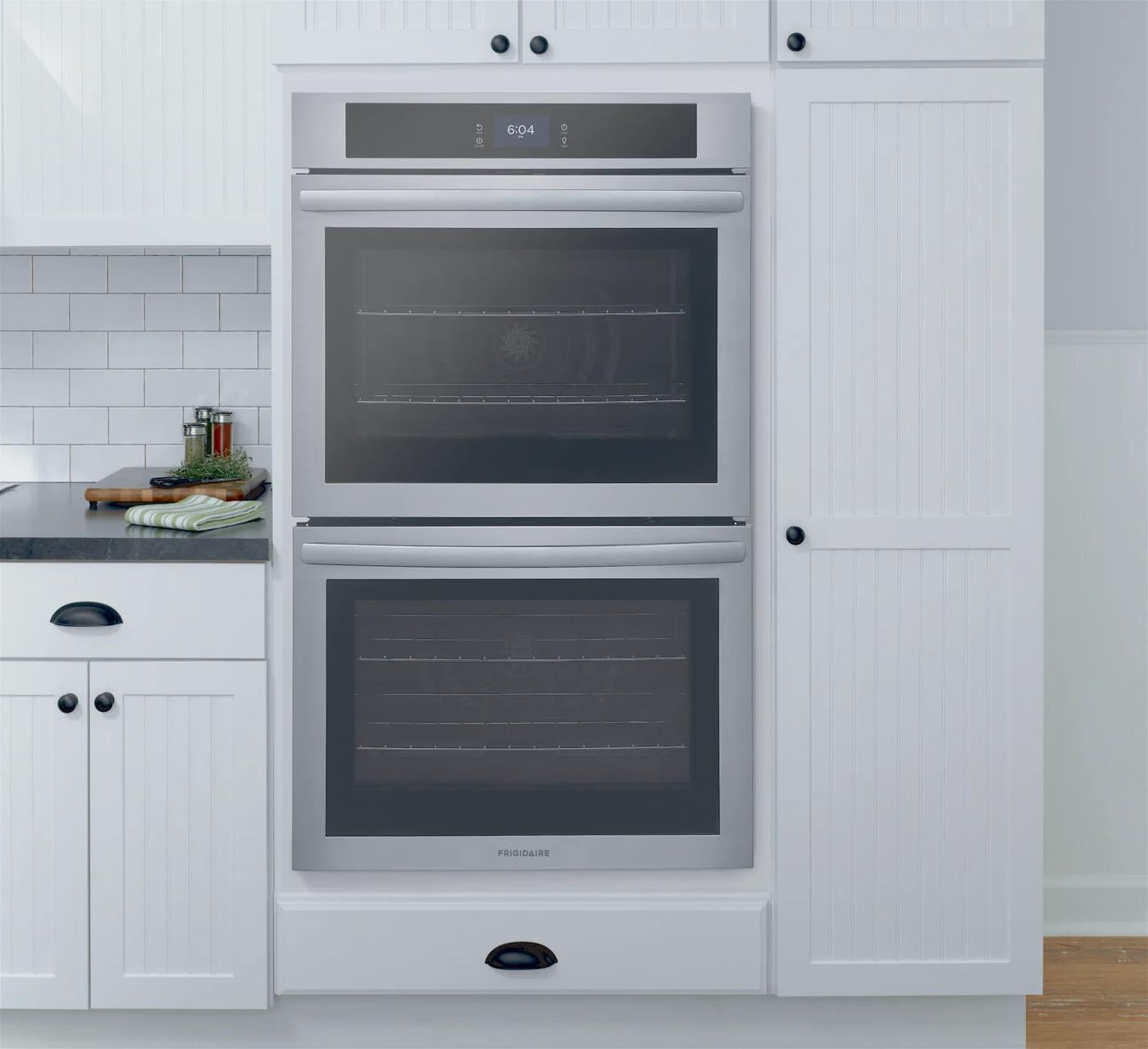 Built-in stainless steel double electric wall oven with fan convection in modern kitchen with white cabinetry and countertop