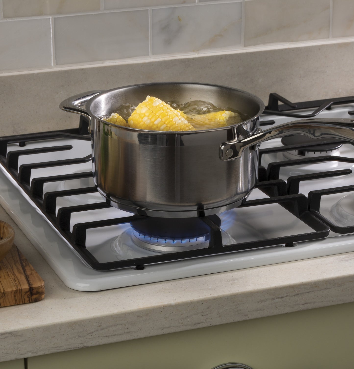 Stainless steel pot boiling corn on the cob on a white built-in gas cooktop in kitchen setting