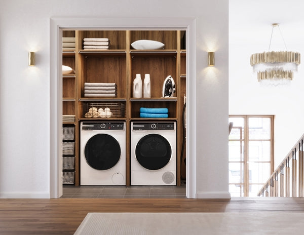 Modern laundry room featuring white front load washer and dryer set with black doors built into wooden shelving unit