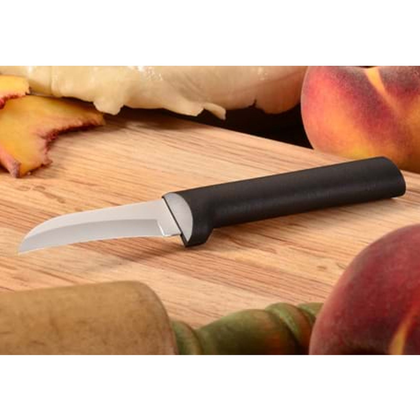 Curved blade paring knife with black handle on wooden cutting board surrounded by fresh peaches in kitchenware collection