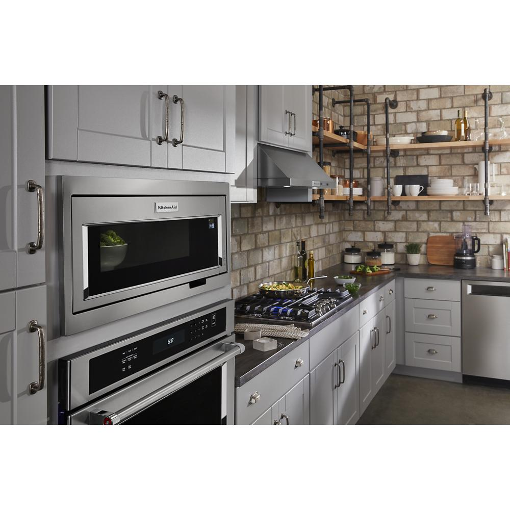 Contemporary kitchen featuring stainless steel microwave, oven, under-cabinet ventilation hood, gray cabinetry, and open wooden shelves