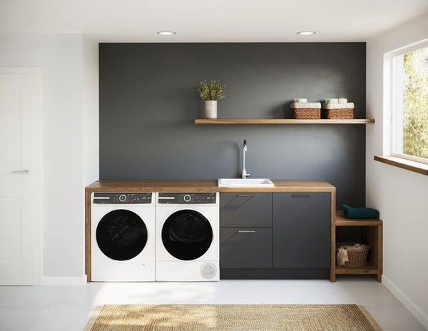 Modern laundry room featuring Bosch front load washer and dryer integrated with wood and dark gray cabinetry and open shelving.