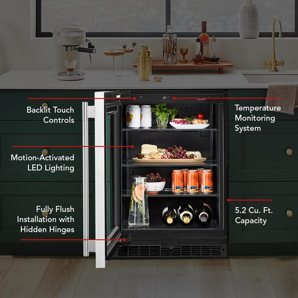 Open undercounter refrigerator with backlit touch controls, LED lighting, stocked with drinks and snacks in dark green kitchen cabinetry