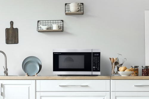 Smart stainless steel countertop microwave oven on white wood kitchen countertop with utensils and shelves