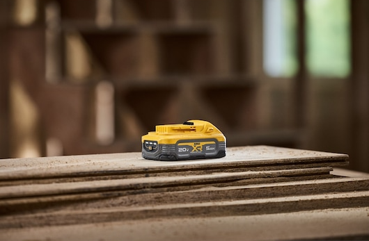 Yellow and gray 20V XR POWERSTACK 5Ah battery resting on stacked wooden boards for tools and home improvement