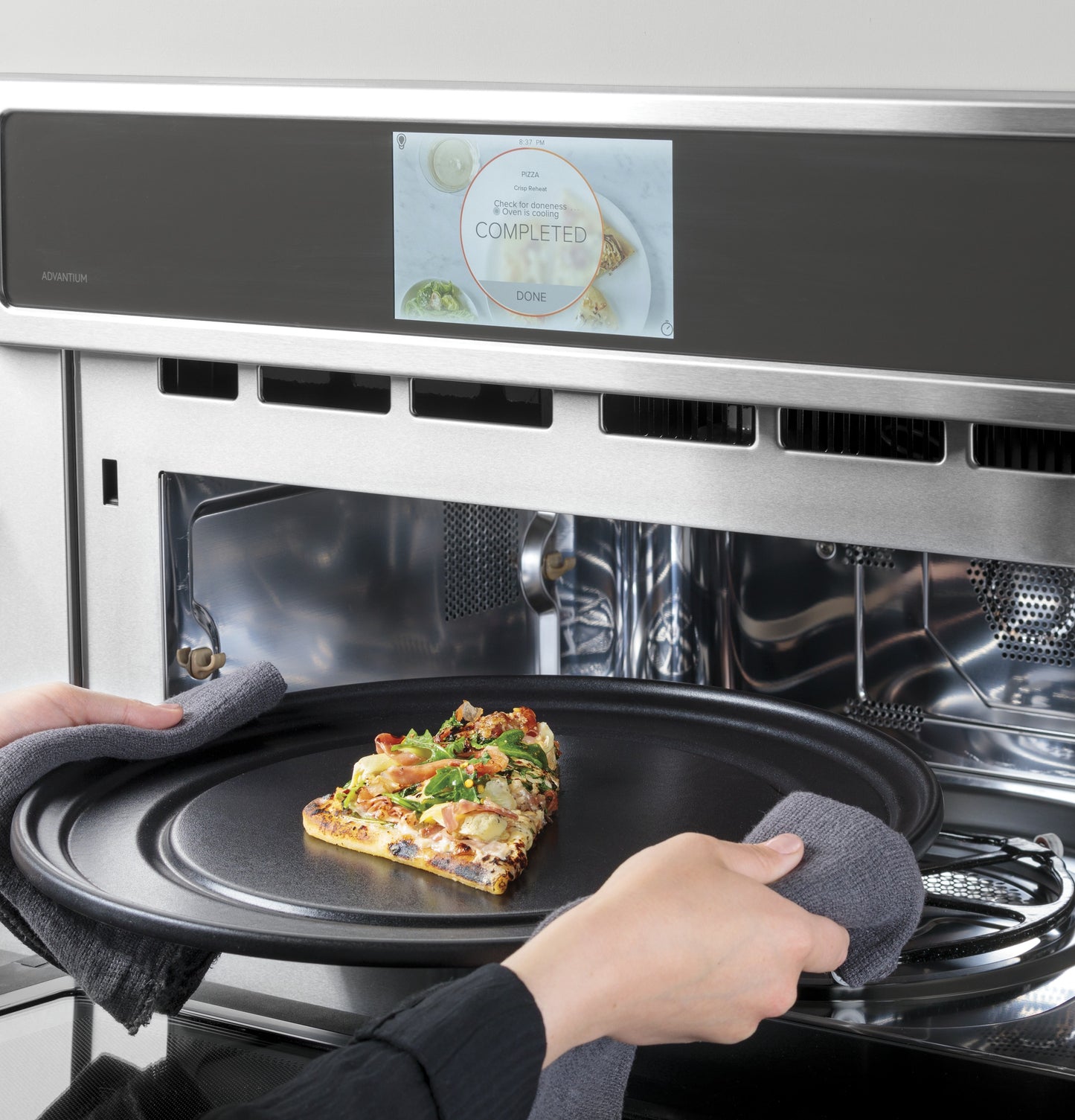 Person removing cooked pizza slice on black tray from stainless steel speed cook oven in Single Wall Ovens collection
