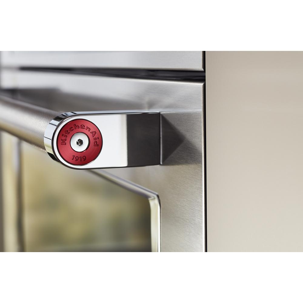 Close-up of brushed stainless steel oven handle with red circular KitchenAid logo accent on the end piece