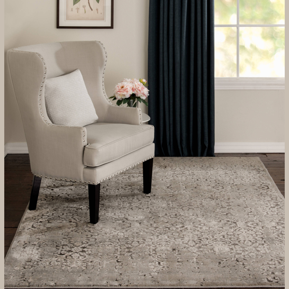 Brown and cream area rug with subtle floral pattern beside beige cushioned armchair in a cozy living room setting