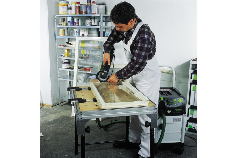 Person using power sander with hard sanding pad on wooden door panel in organized workshop setting
