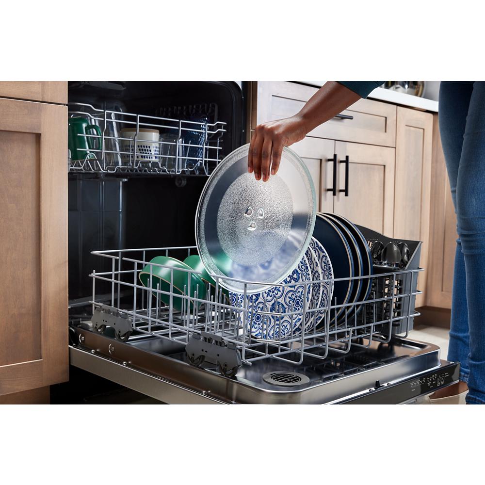 Open dishwasher loaded with patterned plates and glassware being placed inside in modern kitchen setting